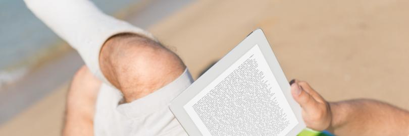 Jemand liegt mit einem Bein im Gips am Strand und liest ein Buch.