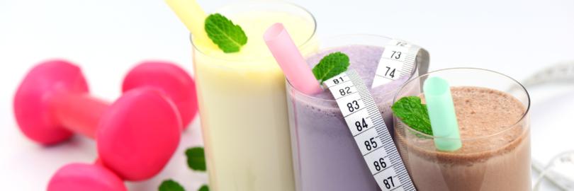 Drei Gläser mit Eiweißshakes stehen nebeneinander, daneben liegen Hanteln.