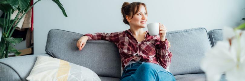 Eine Frau sitz entspannt mit einer Tasse in der Hand auf dem Sofa