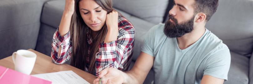 Ein Paar sitzt vor dem Wohnzimmertisch mit Finanzunterlagen und ist unzufrieden