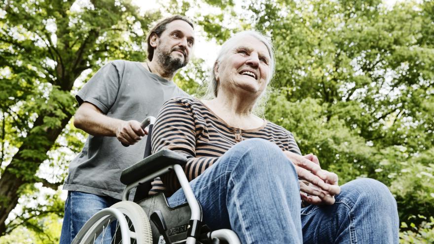 Sohn schiebt demenzkranke Mutter im Rollstuhl.