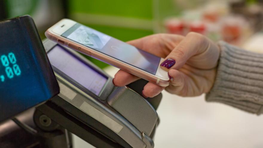 Jemand hält sein Smartphone über ein NFC-Gerät zum Bezahlen an der Kasse.