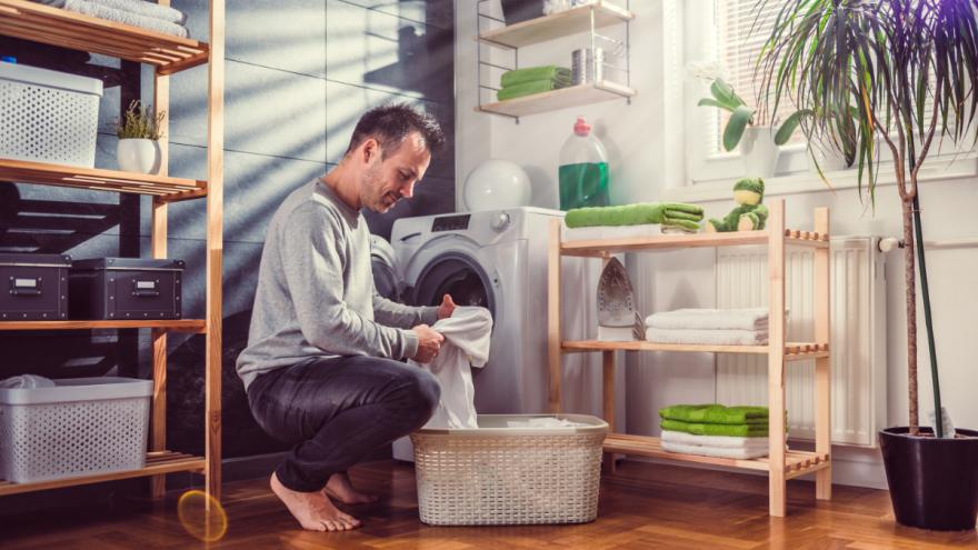 Ein Mann kniet mit Wäsche vor der Waschmaschine.