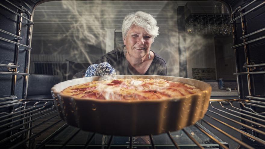 Ältere Frau vor dem Backofen mit Kuchen