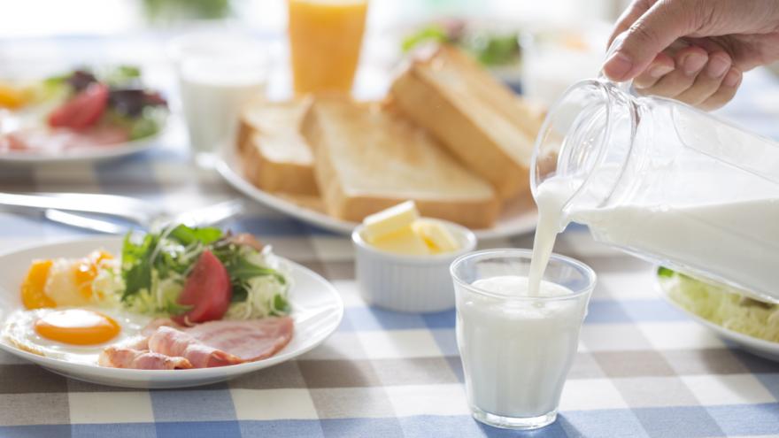 An einem gedeckten Frühstückstisch gießt jemand Milch in ein Glas.