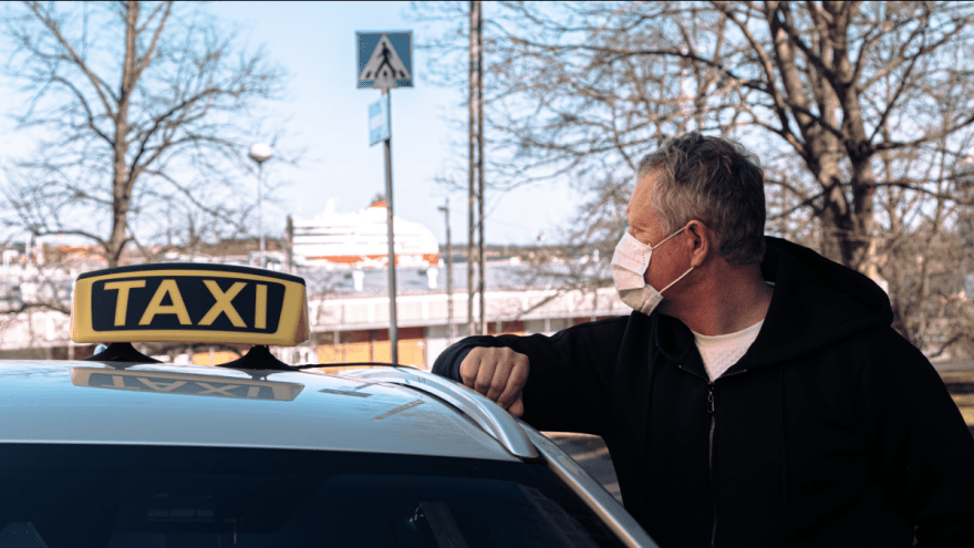 Ein Mann steht an ein Taxi gelehnt und trägt eine Schutzmaske