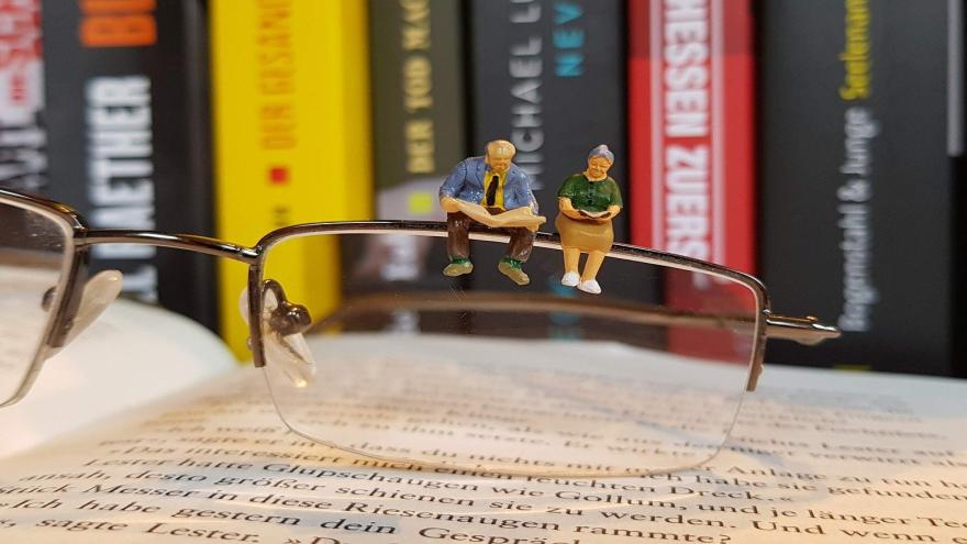 Figuren eines altes Ehepaars sitzt auf einer Brille, die auf Büchern liegt