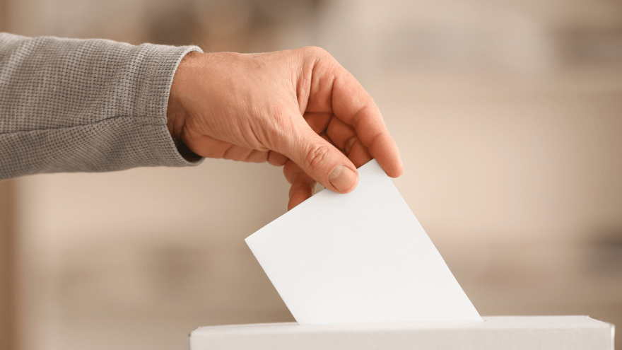 Hand mit Wahlzettel, der in Urne eingeworfen wird