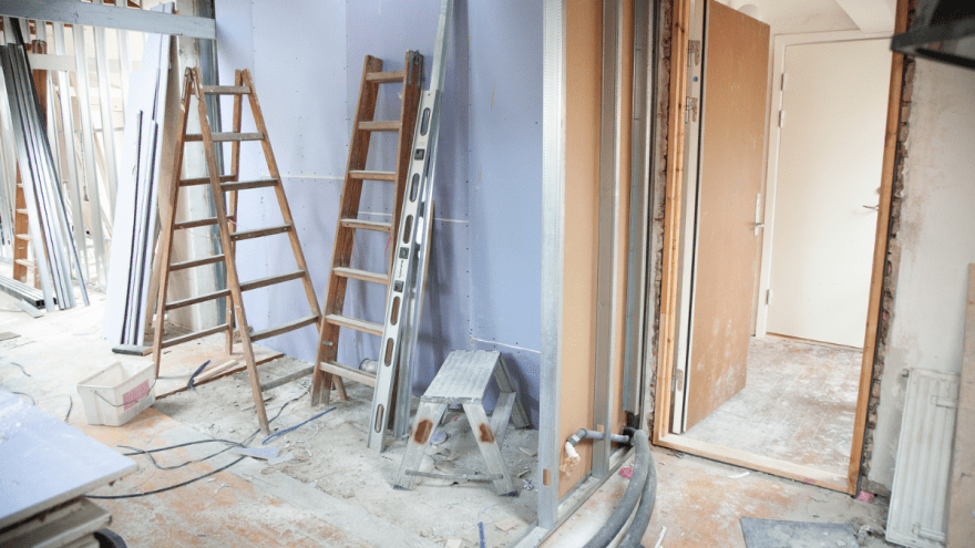Leitern und Werkzeuge lehnen an einer Wand in einem Zimmer, das im Rohbau ist