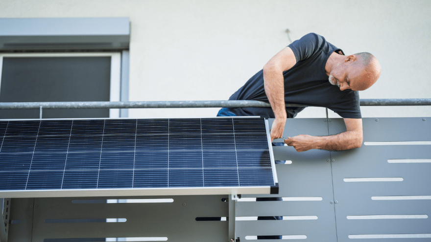 Mann schraubt Stecker-PV-Anlage an Balkon an