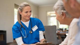 Eine Pflegerin spricht mit einem Seniorenpaar