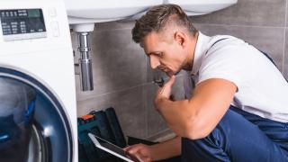 Ein Installateur kontrolliert den Wasseranschluss einer Waschmaschine