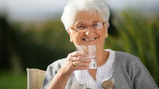 Seniorin hält Glas Wasser in der Hand und lächelt