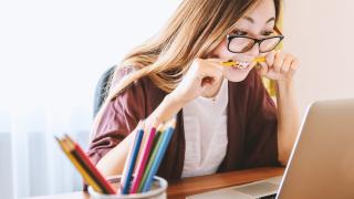 Frau vor Laptop beißt in Stift