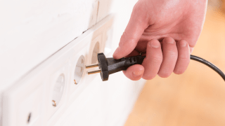 Hand, die einen Stecker aus der Steckdose zieht