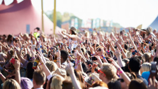 Hunderte Musikfans vor einer Bühne, die ihre Arme in Luft heben