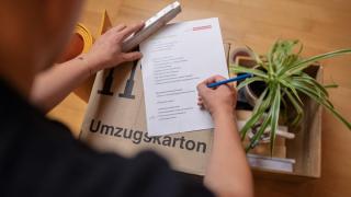 Mann schreibt Liste auf Umzugskarton