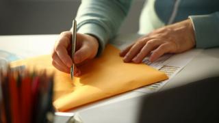 Briefe beschriften: Jemand schreibt eine Adresse auf einen gelben Briefumschlag