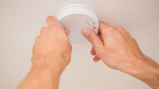 Zwei Hände arbeiten an einem Rauchmelder an der Decke