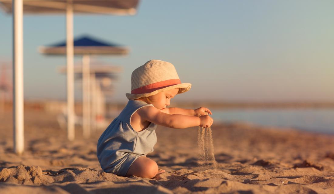 Ein Kind spielt am Strand im Sand und trägt einen Hut gegen die Sonne