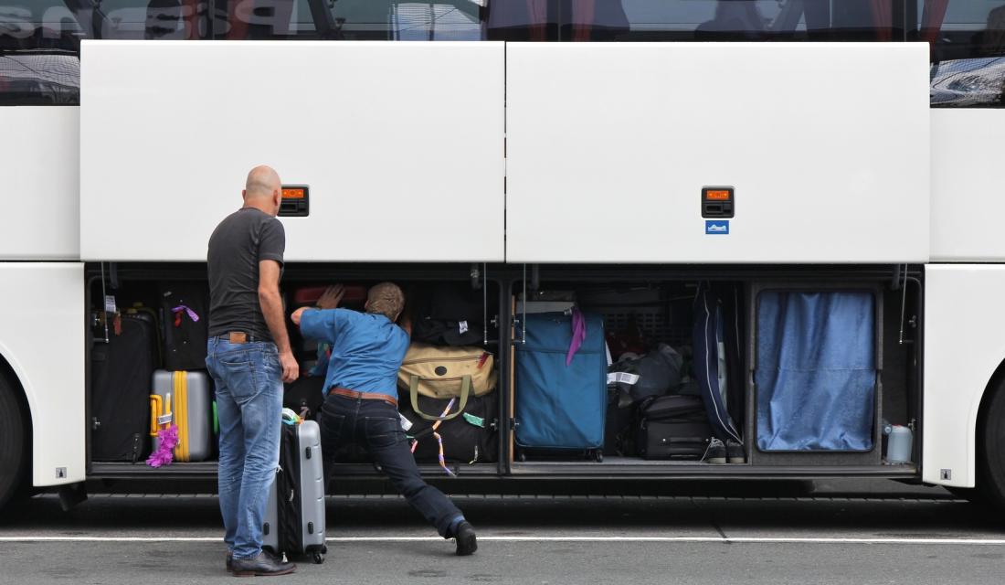 Reisende packen ihr Gepäck in einen Fernbus.